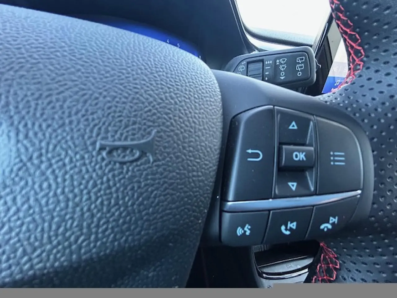 Gros plan sur le volant cuir perforé avec surpiqûres rouges du Ford Puma gris Magnetic, boutons de commande intégrés visibles.