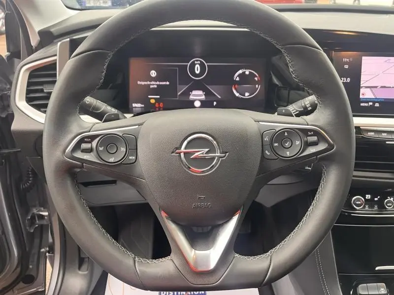 Vue intérieure centrée sur le volant cuir multifonction d'un Opel Grandland gris, avec écran tactile et commandes au volant visibles.