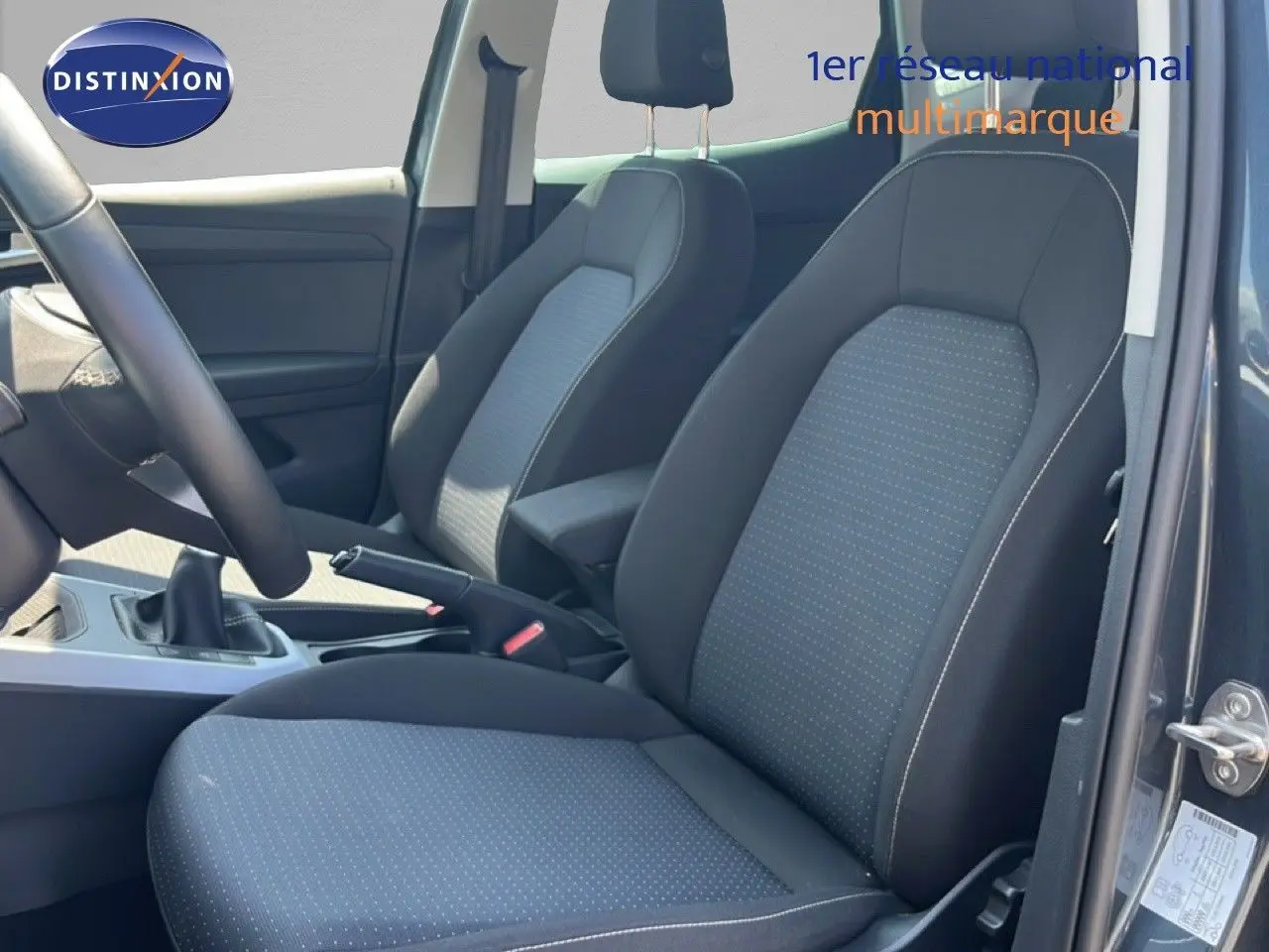 Vue intérieure côté conducteur du SEAT Arona 2025, sièges tissu gris à motifs et volant cuir multifonction.