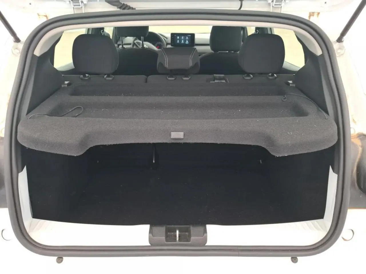 Vue arrière du coffre ouvert d'une Dacia Sandero blanche 2024, avec tablette cache-bagages et sièges arrière visibles.
