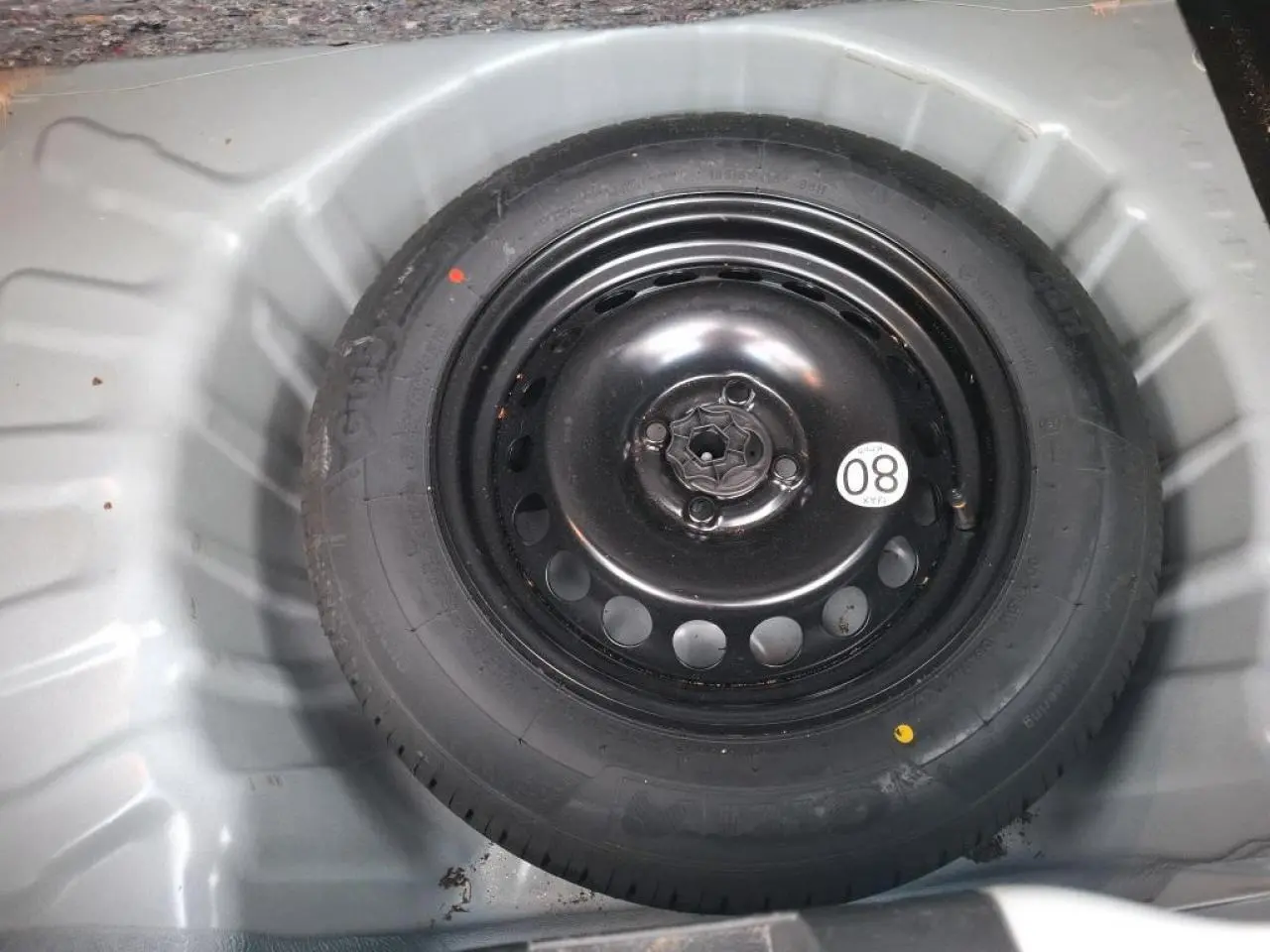Gros plan sur la roue de secours noire dans le coffre d'une Dacia Sandero blanche 2024.