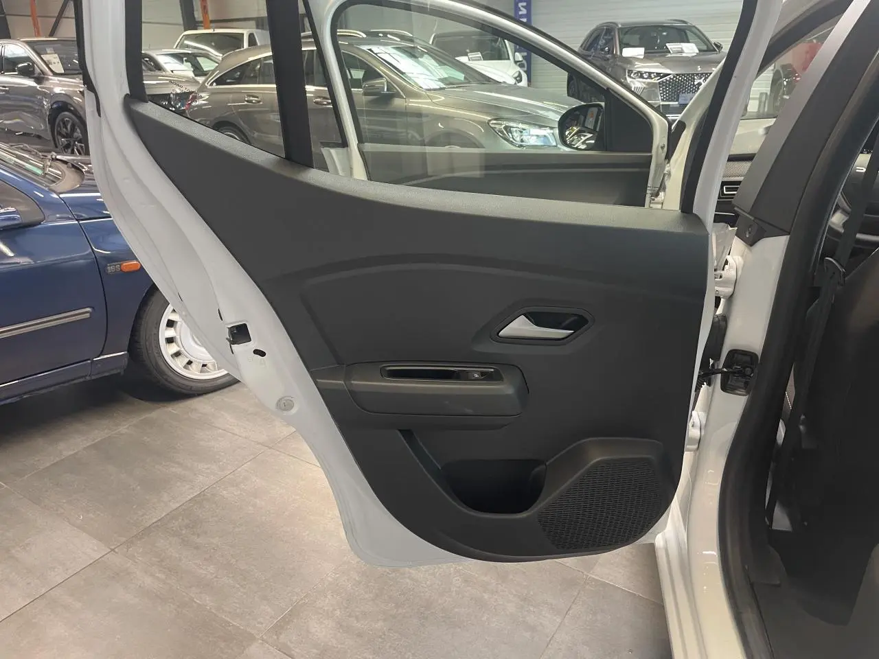 Vue intérieure de la porte arrière droite noire d'une Dacia Sandero blanche 2024 avec poignée argentée.