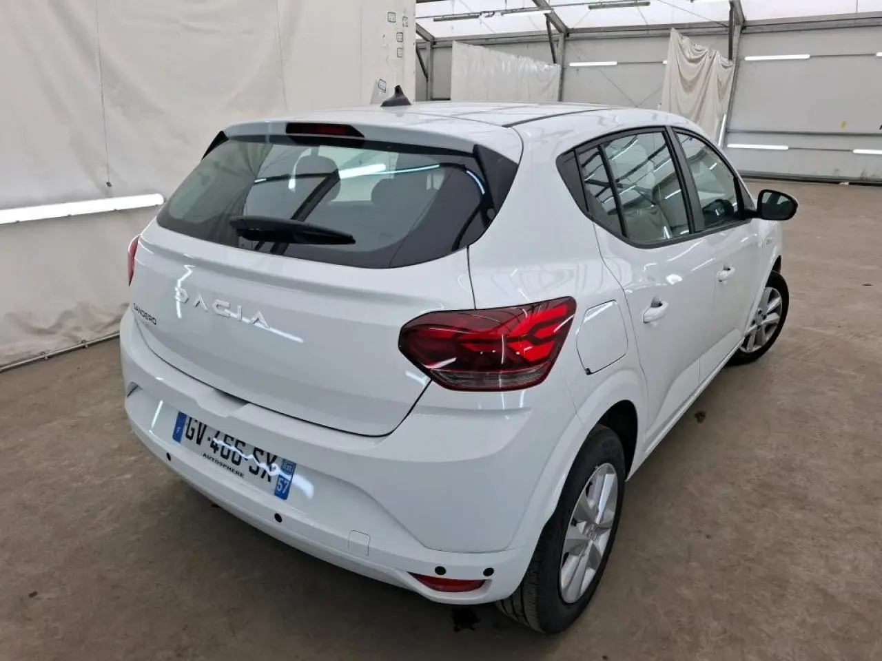 Vue 3/4 arrière droite d'une Dacia Sandero blanche 2024 avec feux arrière LED et jantes à enjoliveurs.