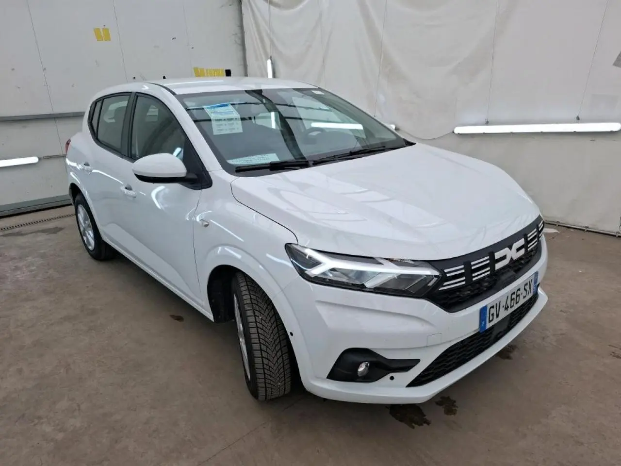 Dacia Sandero blanc vue 3/4 avant droit, avec calandre noire et signature lumineuse LED distinctives.