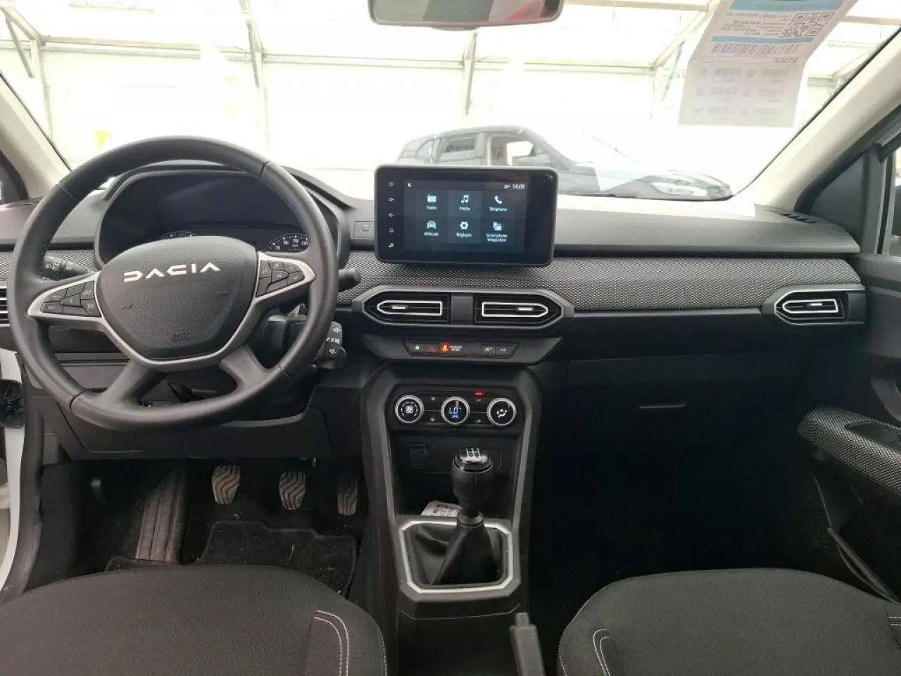 Vue intérieure avant de la Dacia Sandero blanche 2024, tableau de bord avec écran tactile et volant multifonction.
