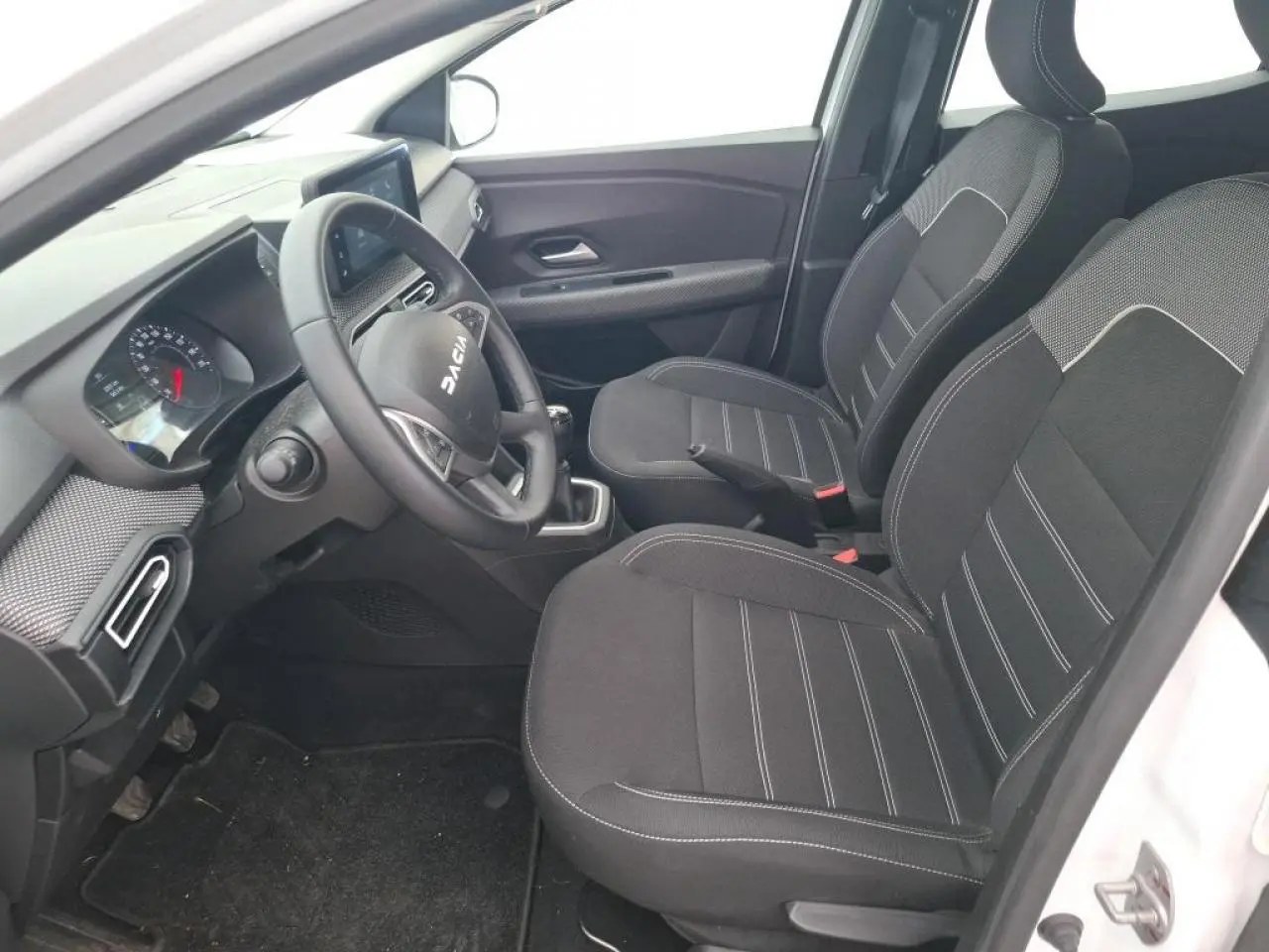 Vue intérieure côté conducteur de la Dacia Sandero blanche 2024, avec sellerie tissu noire et volant multifonction.