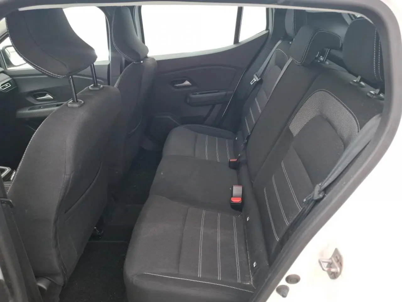 Vue intérieure côté droit sur la banquette arrière noire avec surpiqûres blanches d'une Dacia Sandero blanche 2024.