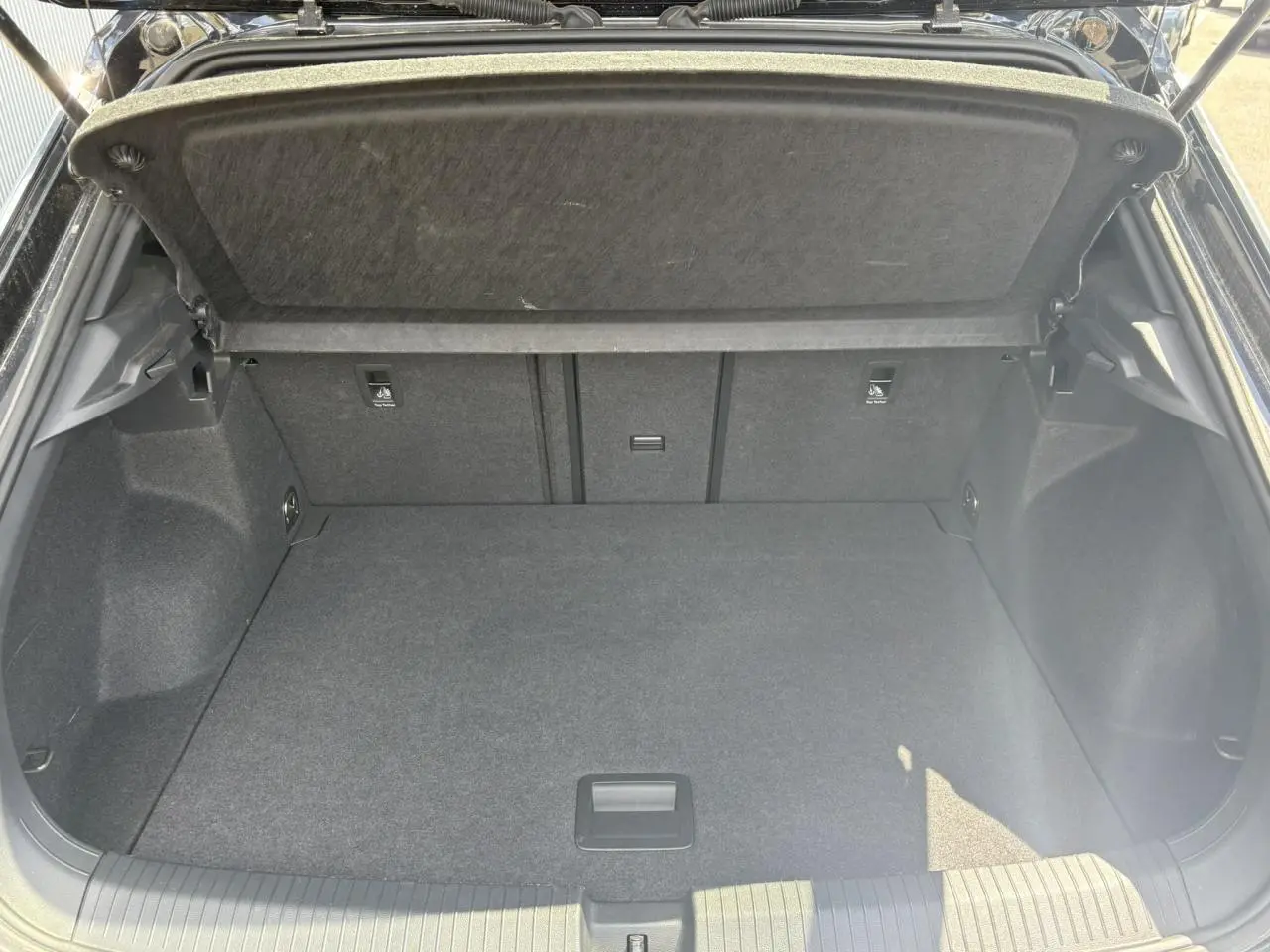 Coffre ouvert du Volkswagen T-Roc noir intense 2025, vue arrière montrant l'espace de chargement vide et le cache-bagages relevé.