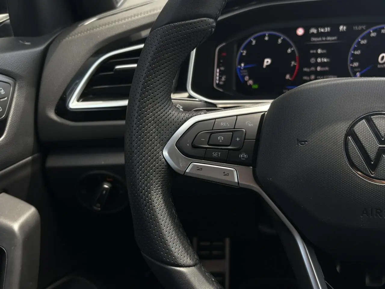 Vue rapprochée du volant cuir perforé côté gauche avec commandes régulateur adaptatif et tableau de bord digital du Volkswagen T-Roc noir intense 2025.