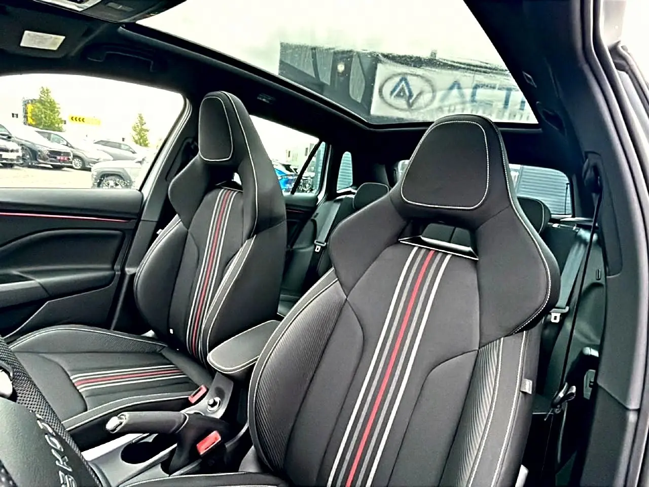 Vue intérieure des sièges avant sport noirs avec surpiqûres blanches et bandes rouges du Skoda Kamiq Monte Carlo 2026, toit panoramique visible.