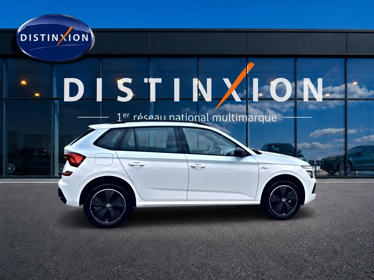Vue latérale droite d'un Skoda Kamiq blanc nacre avec jantes noires devant une vitrine Distinxion.