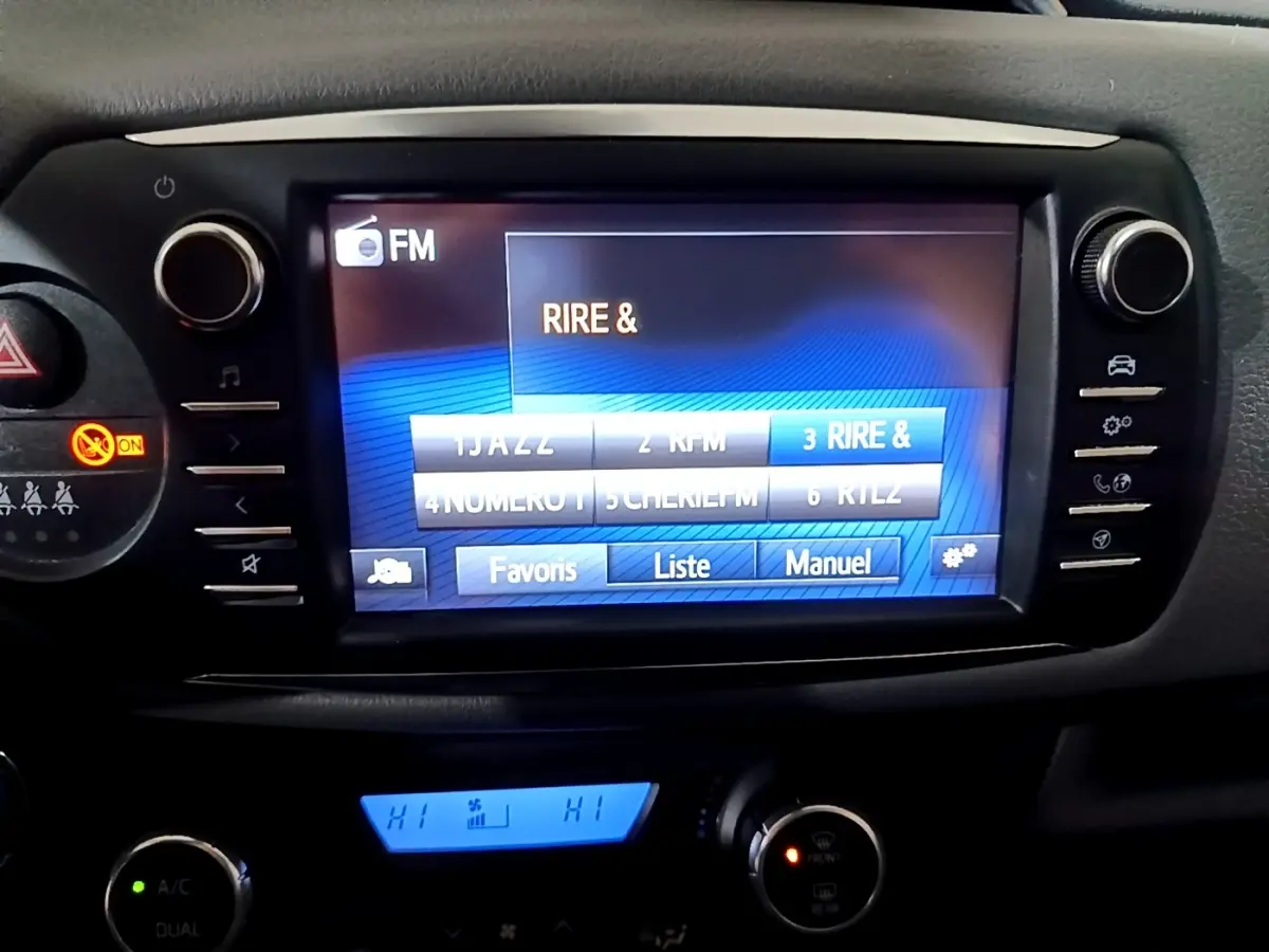 Écran tactile central de la Toyota Yaris hybride 2019 affichant les stations FM, avec commandes climatisation en dessous.
