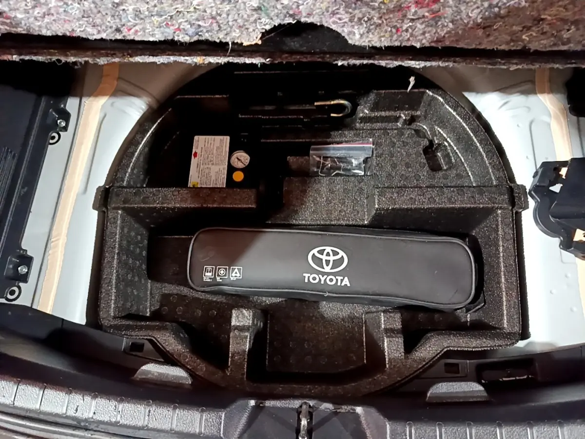 Vue plongeante sur le coffre ouvert d'une Toyota Yaris blanche, montrant le rangement sous tablette avec kit de secours Toyota.