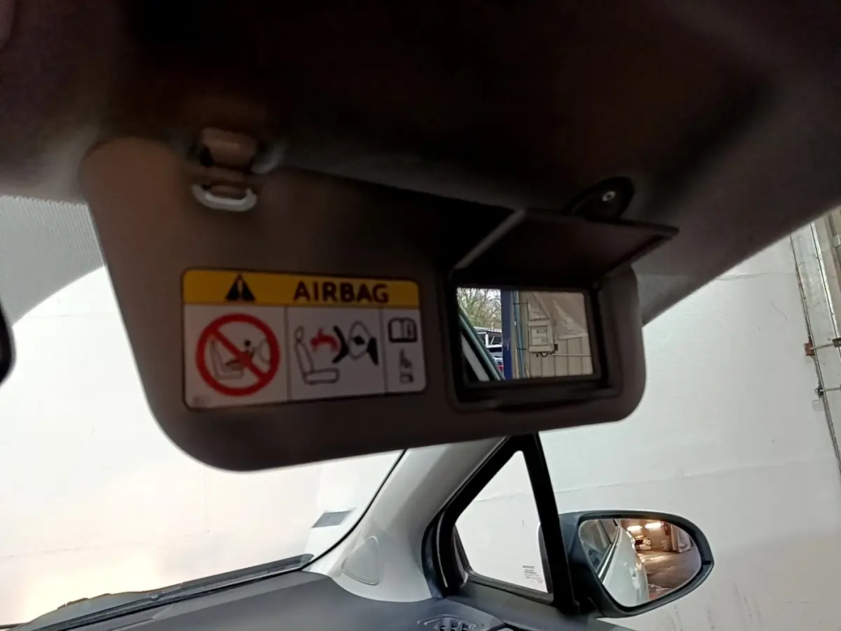 Détail du pare-soleil avec miroir et avertissement airbag, vue intérieure côté conducteur d'une Toyota Yaris blanche.