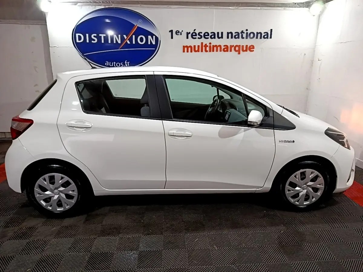 Profil droit d'une Toyota Yaris blanche 2019 hybride, avec jantes standard et logo Hybrid visible sur l'aile avant.