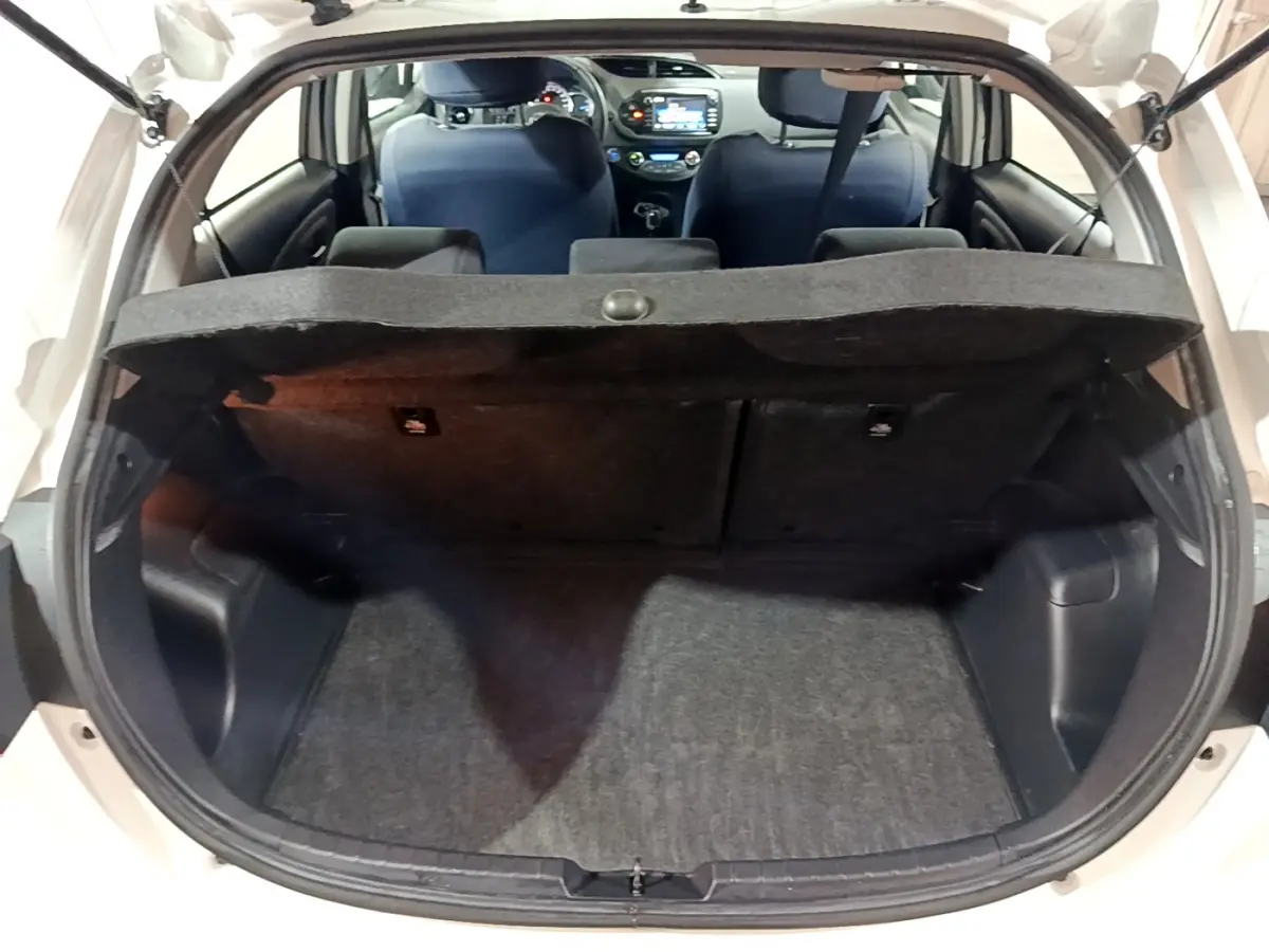 Coffre ouvert vu de l'arrière d'une Toyota Yaris blanche, intérieur noir avec tablette cache-bagages et sièges avant visibles.