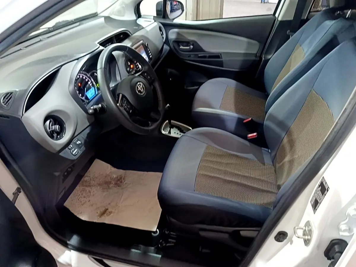 Intérieur côté conducteur d'une Toyota Yaris blanche 2019, montrant sièges tissu bleu et tableau de bord avec écran tactile.