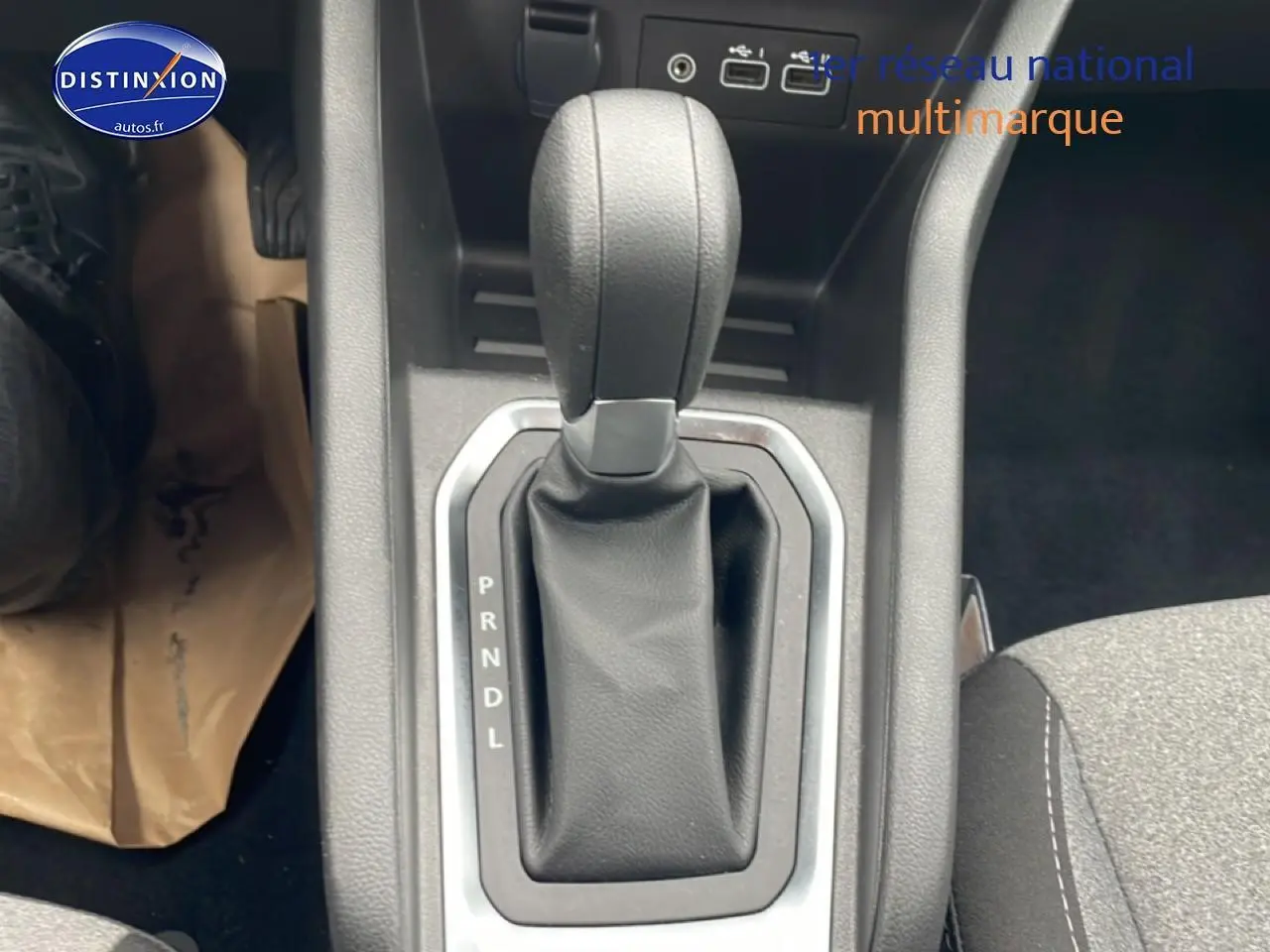 Gros plan sur le levier de vitesse automatique noir de la Renault Clio V essence, intérieur tissu gris visible à droite.