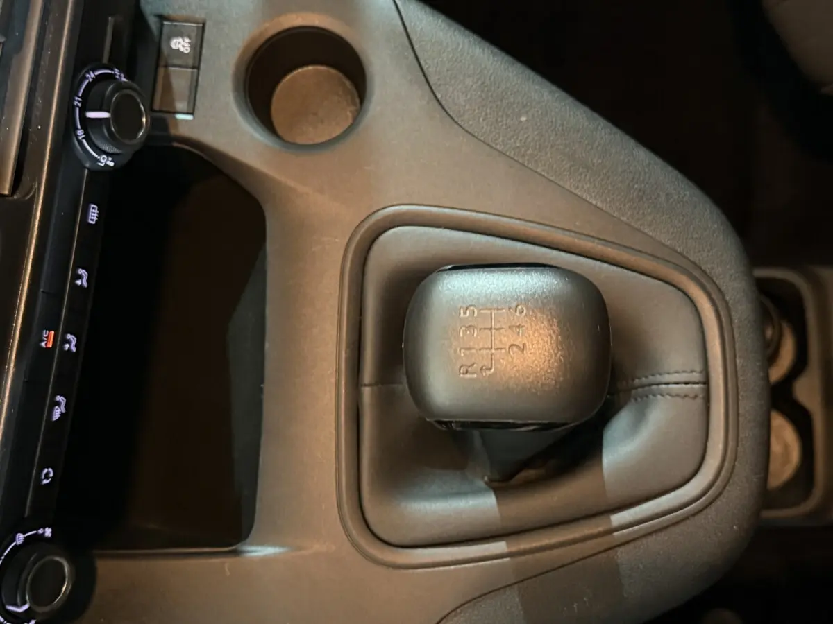 Gros plan sur le levier de vitesses manuel noir du Peugeot Rifter blanc, avec console centrale et commandes climatisation visibles.