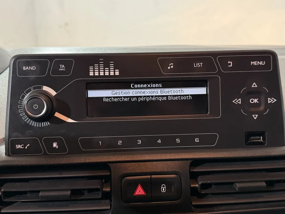 Vue rapprochée du tableau de bord du Peugeot Rifter blanc 2019, affichage Bluetooth et commandes audio visibles.