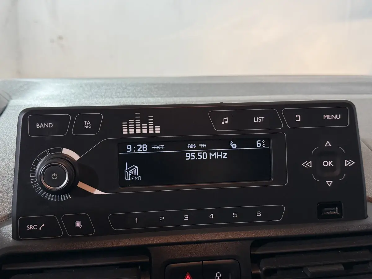 Gros plan sur l'autoradio noir du Peugeot Rifter blanc, affichant la fréquence FM 95,50 MHz et la température extérieure 6°C.