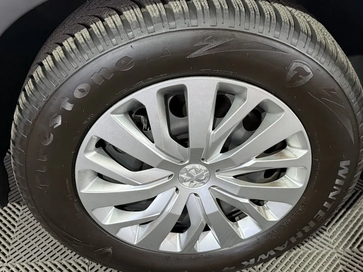 Gros plan sur la roue avant droite du Peugeot Rifter blanc, mettant en valeur la jante argentée et le pneu Firestone.