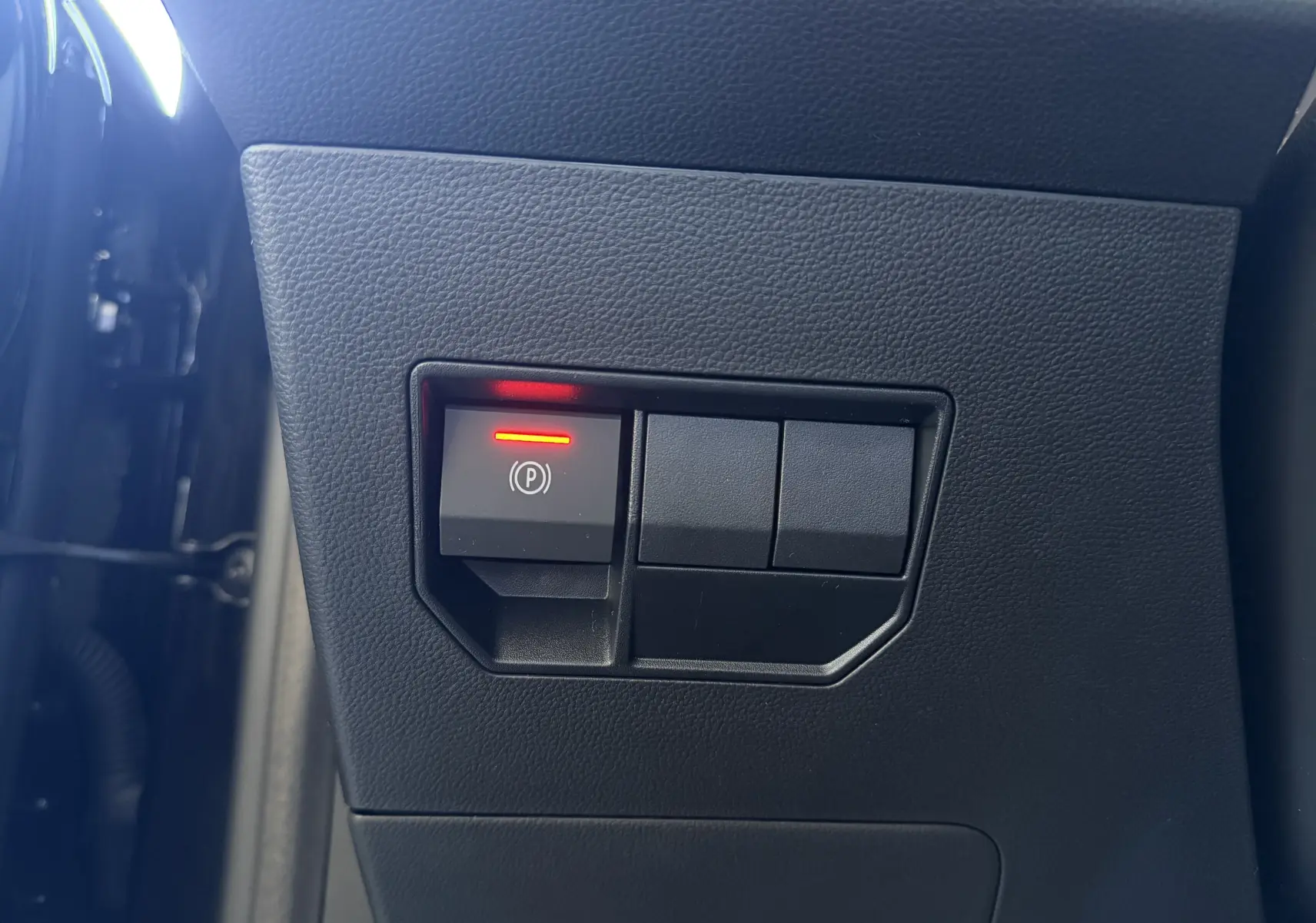 Gros plan sur le bouton de frein à main électrique allumé, intégré dans le tableau de bord noir du Dacia Duster Hybrid 155.