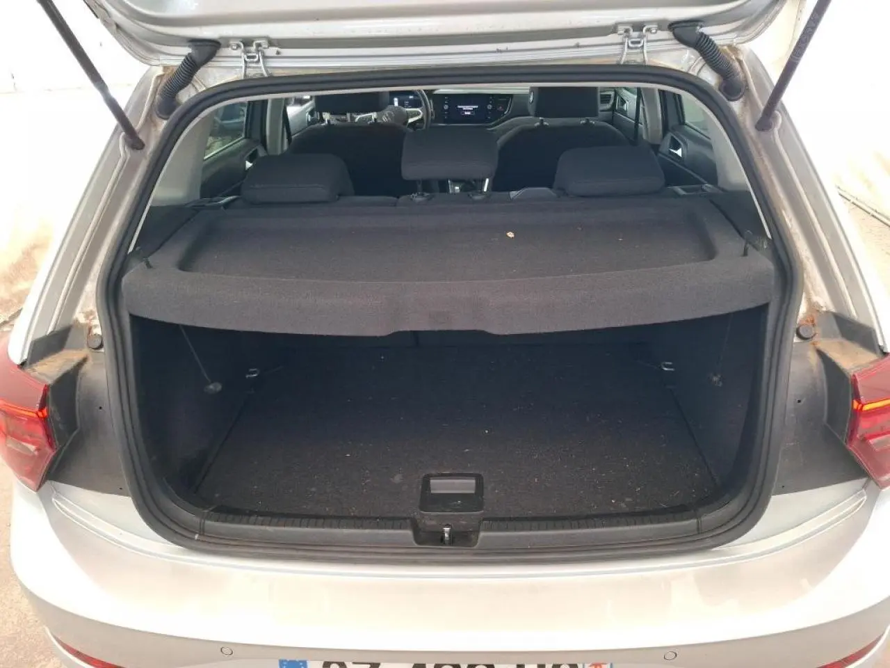 Coffre ouvert d'une Volkswagen Polo gris clair vue de l'arrière, avec tablette cache-bagages et intérieur sombre visible.