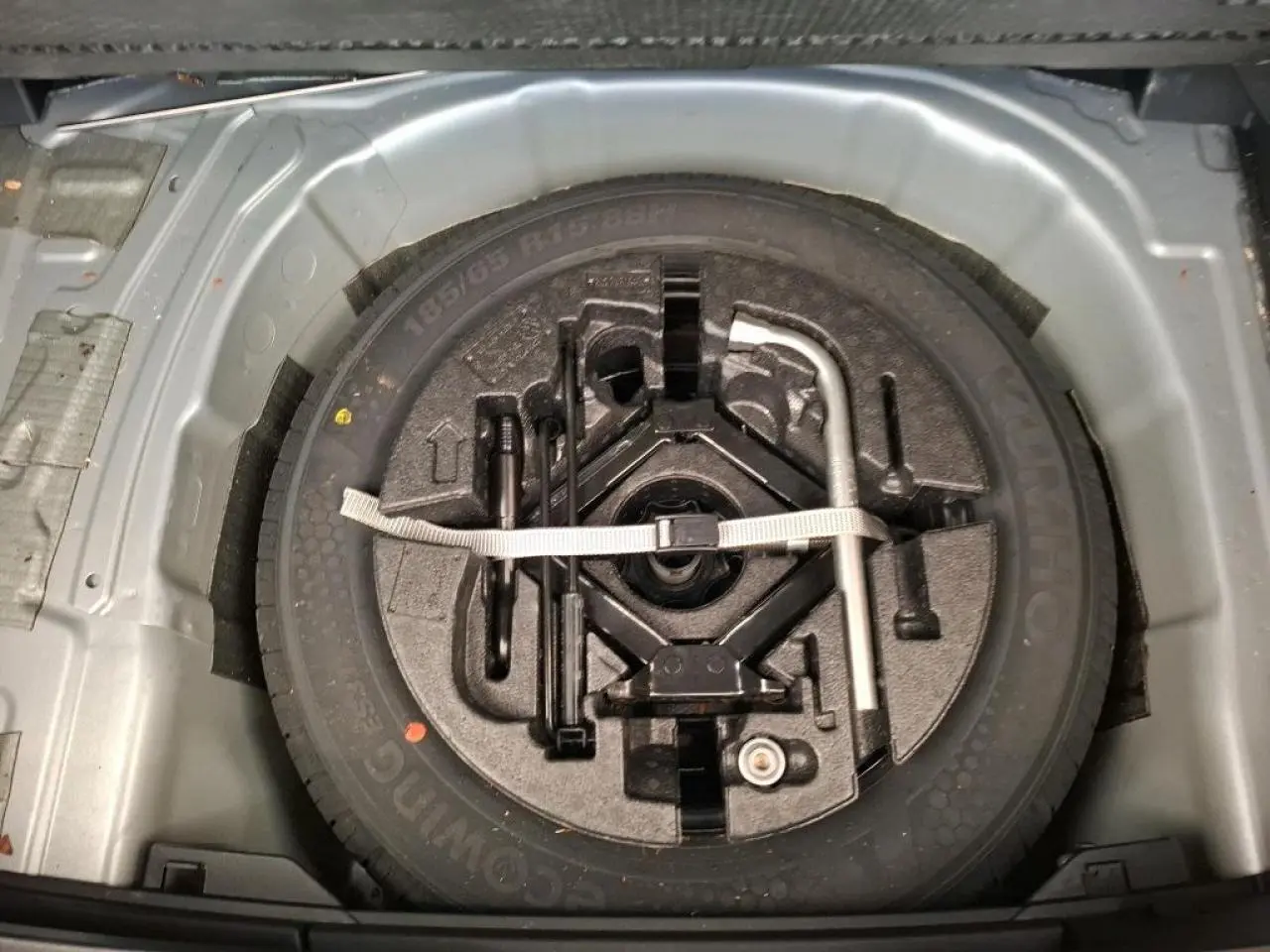 Vue plongeante sur la roue de secours acier 15 pouces et outillage de bord dans le coffre d'une Volkswagen Polo gris clair.