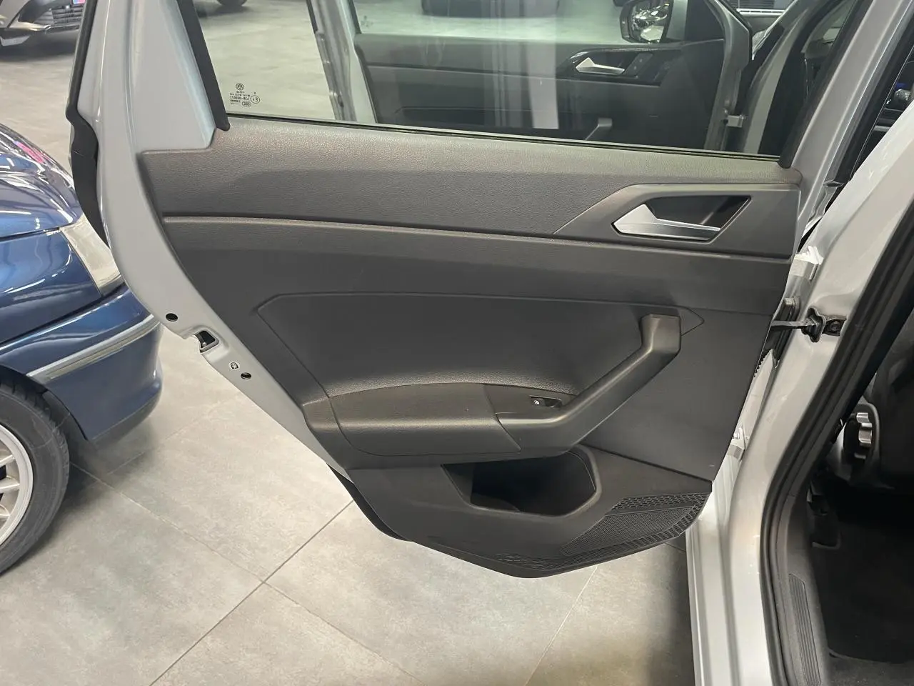 Vue rapprochée de la porte arrière droite gris clair de la Volkswagen Polo 2024, avec poignée intérieure et commande de vitre.