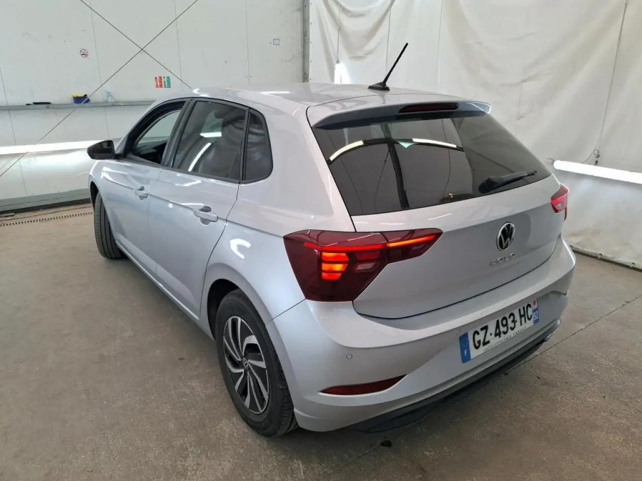 Volkswagen Polo gris clair vue 3/4 arrière droit avec feux arrière allumés dans un garage.