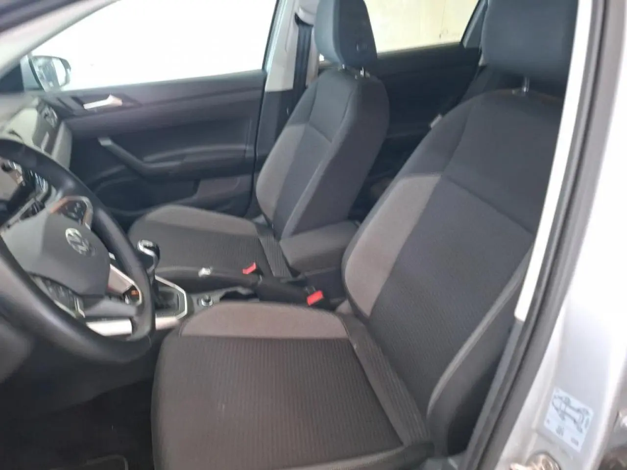 Vue intérieure côté conducteur de la Volkswagen Polo 2024, sièges tissu gris foncé avec accoudoir central.
