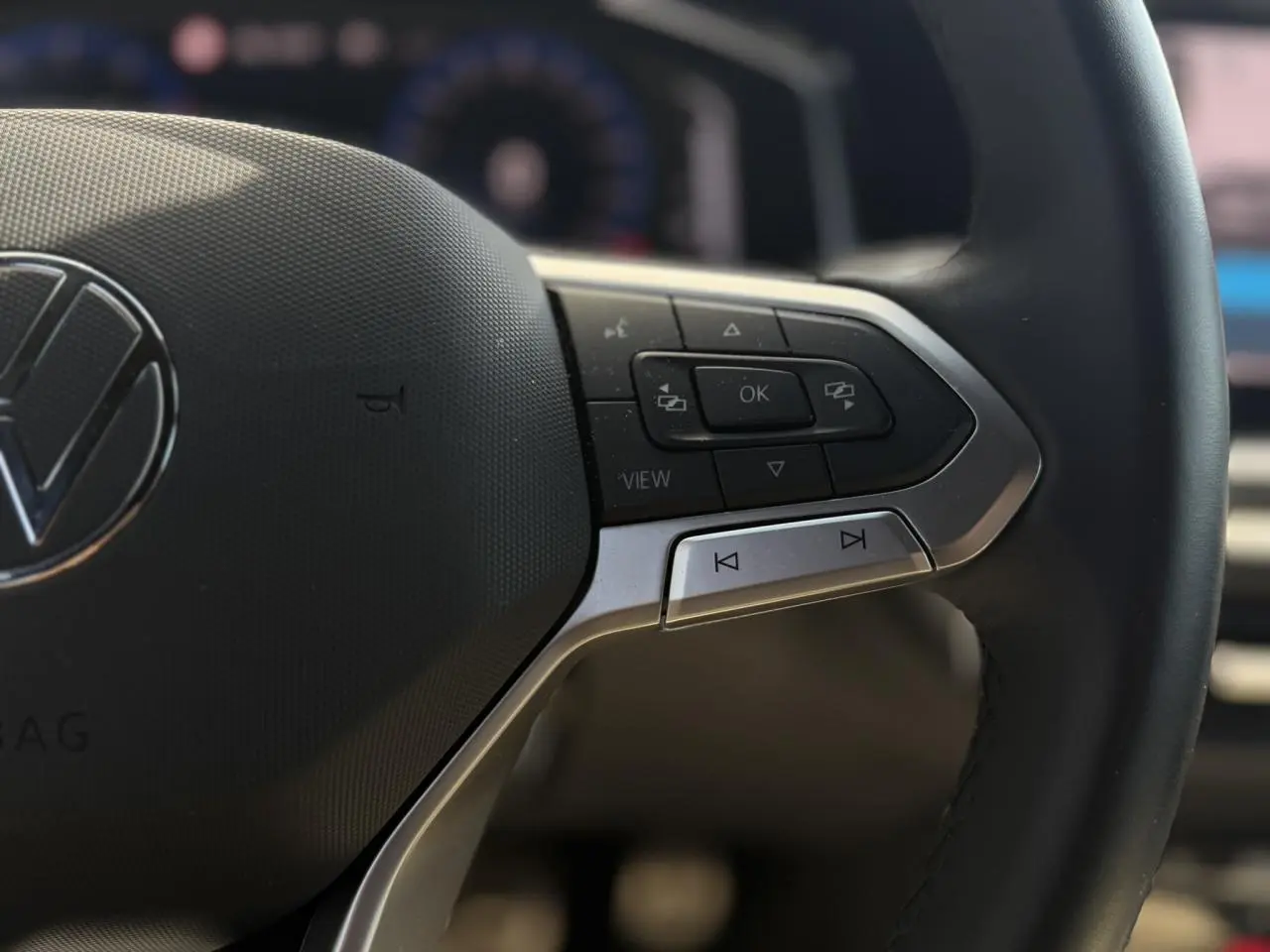Gros plan sur le volant cuir noir du Volkswagen Taigo 2025, avec commandes multifonctions et logo VW central.