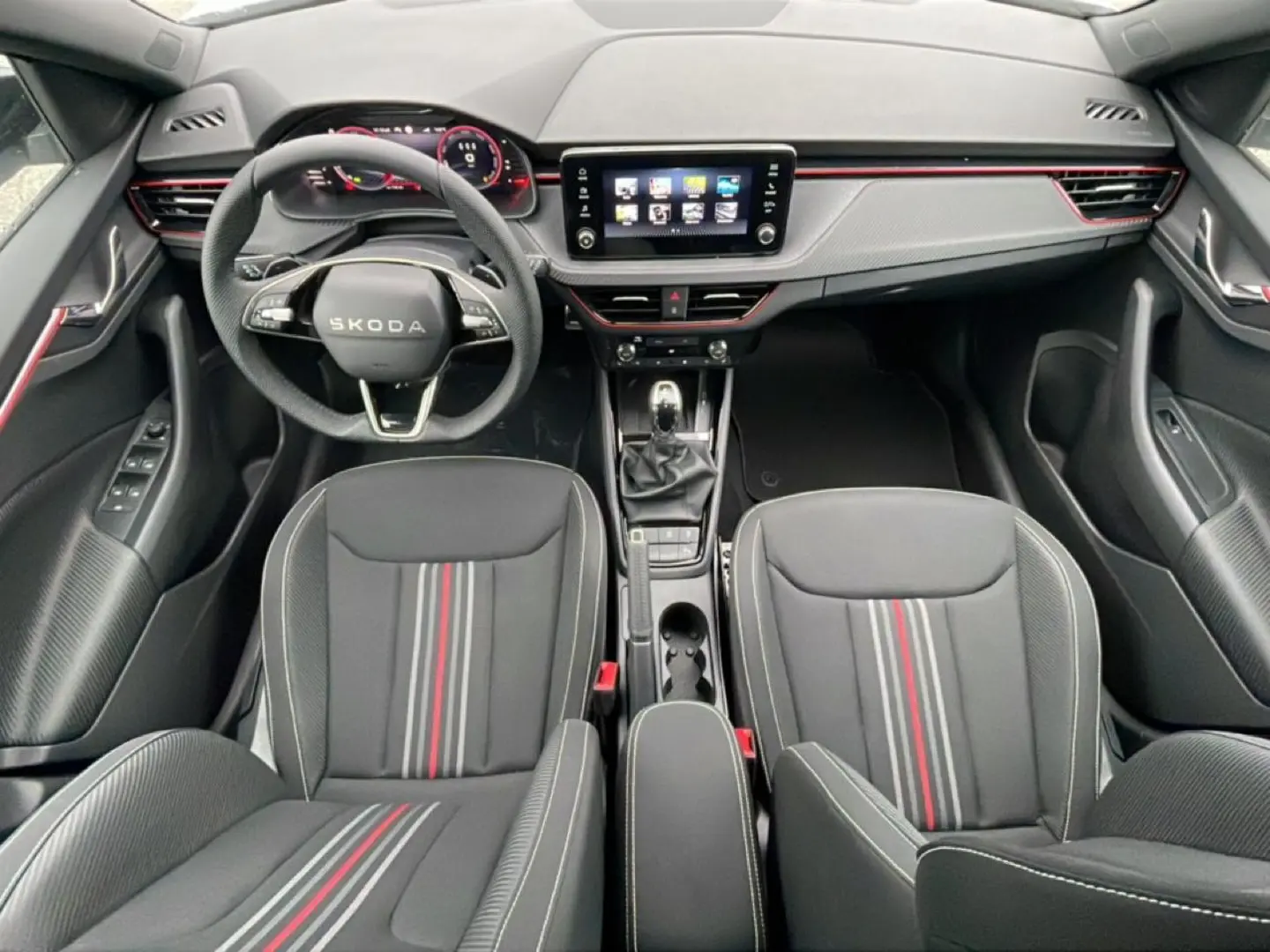 Vue intérieure avant du Skoda Kamiq Monte Carlo 2026, sièges noirs avec bandes rouges et tableau de bord moderne.