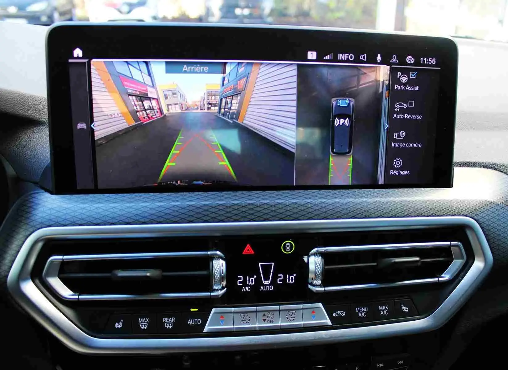 Vue intérieure du tableau de bord du BMW X3 xDrive 30e 2023 avec écran d'aide au stationnement et commandes climatisation.