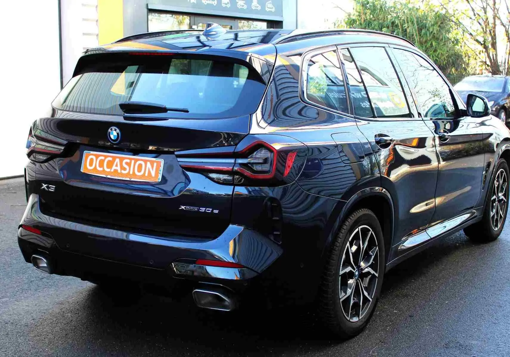 Vue 3/4 arrière droite d'un BMW X3 xDrive 30e hybride rechargeable bleu métal avec jantes M Sport en 2023.