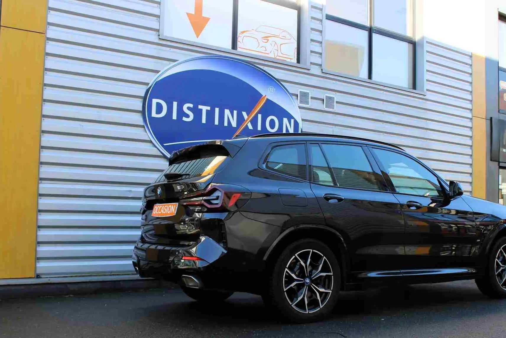 Vue 3/4 arrière d'un BMW X3 xDrive bleu métal 2023 avec jantes sport et badge hybride rechargeable visible.