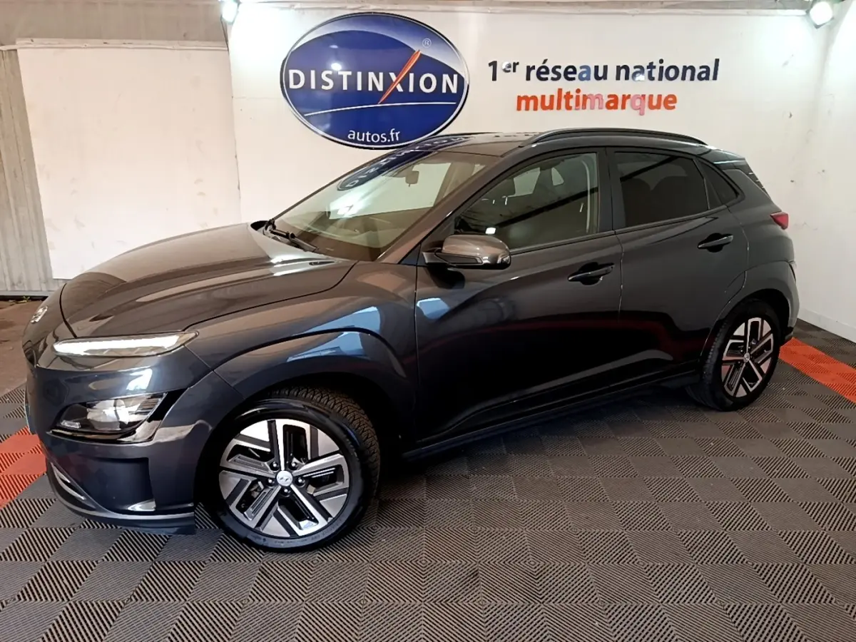 Hyundai Kona électrique 2021 gris foncé en 3/4 avant droit, avec jantes spécifiques et rails de toit noirs visibles.