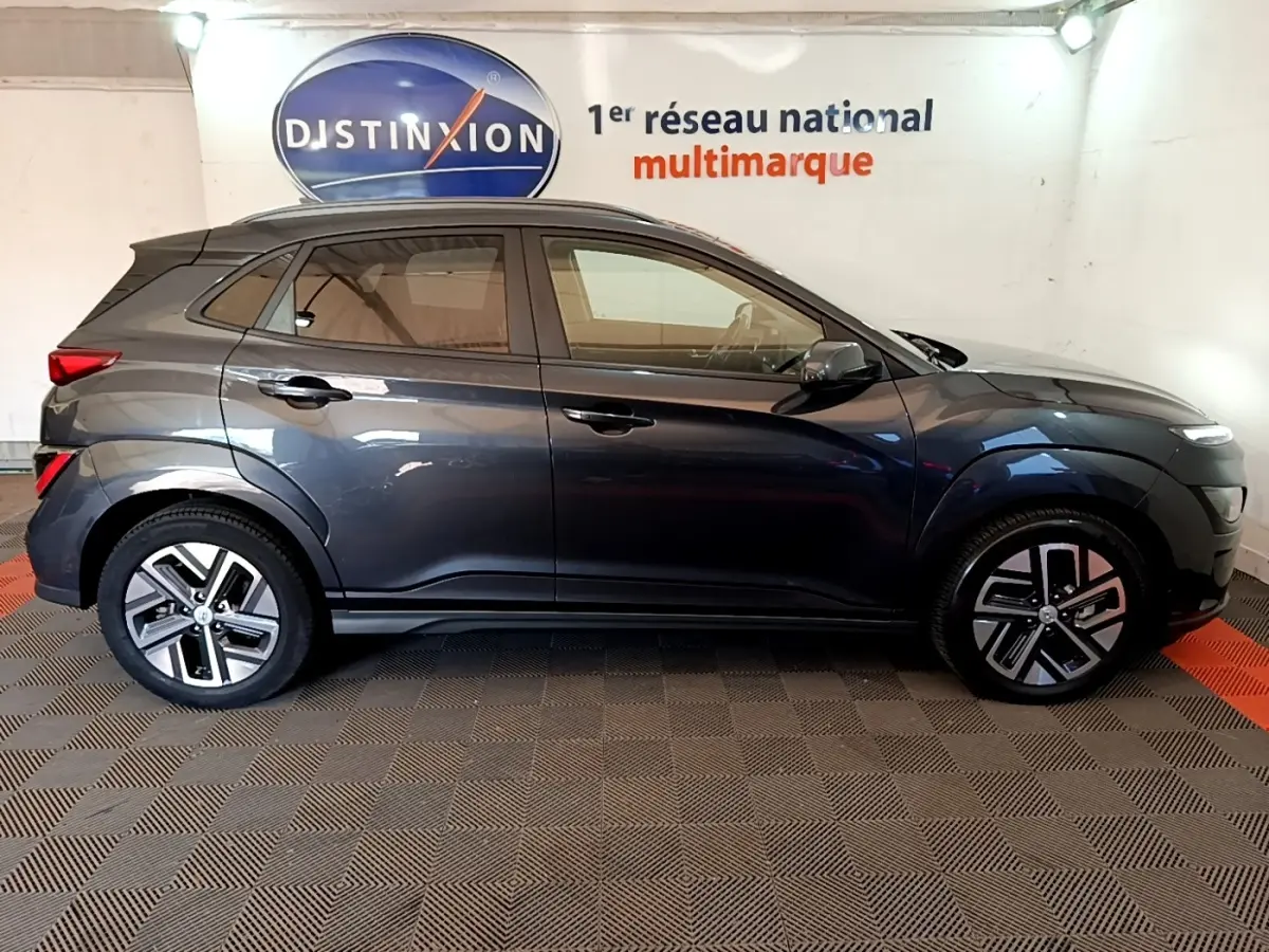 Vue de profil côté gauche d'un Hyundai Kona électrique gris foncé stationné en intérieur avec jantes distinctives.
