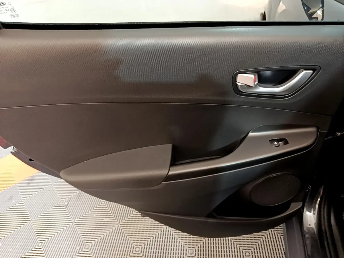 Vue intérieure côté gauche de la porte avant noire du Hyundai Kona électrique avec poignée argentée et commande de vitre.