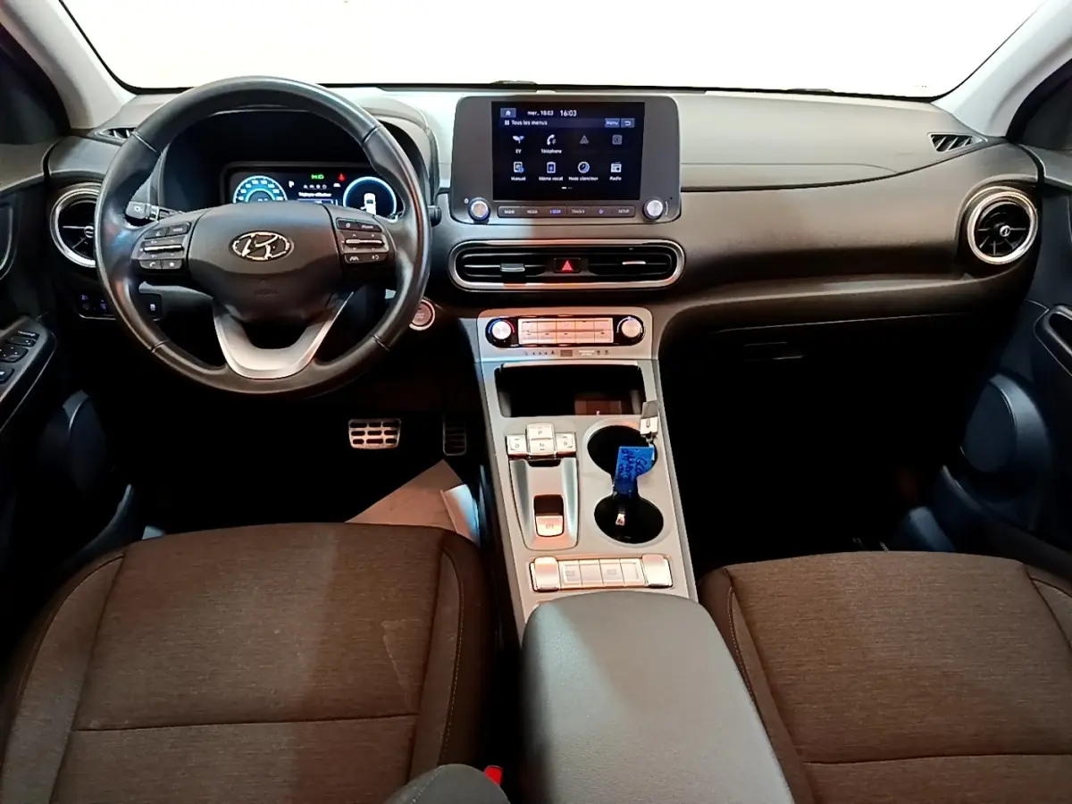 Vue intérieure frontale du tableau de bord et volant cuir noir de la Hyundai Kona électrique avec écran tactile central.