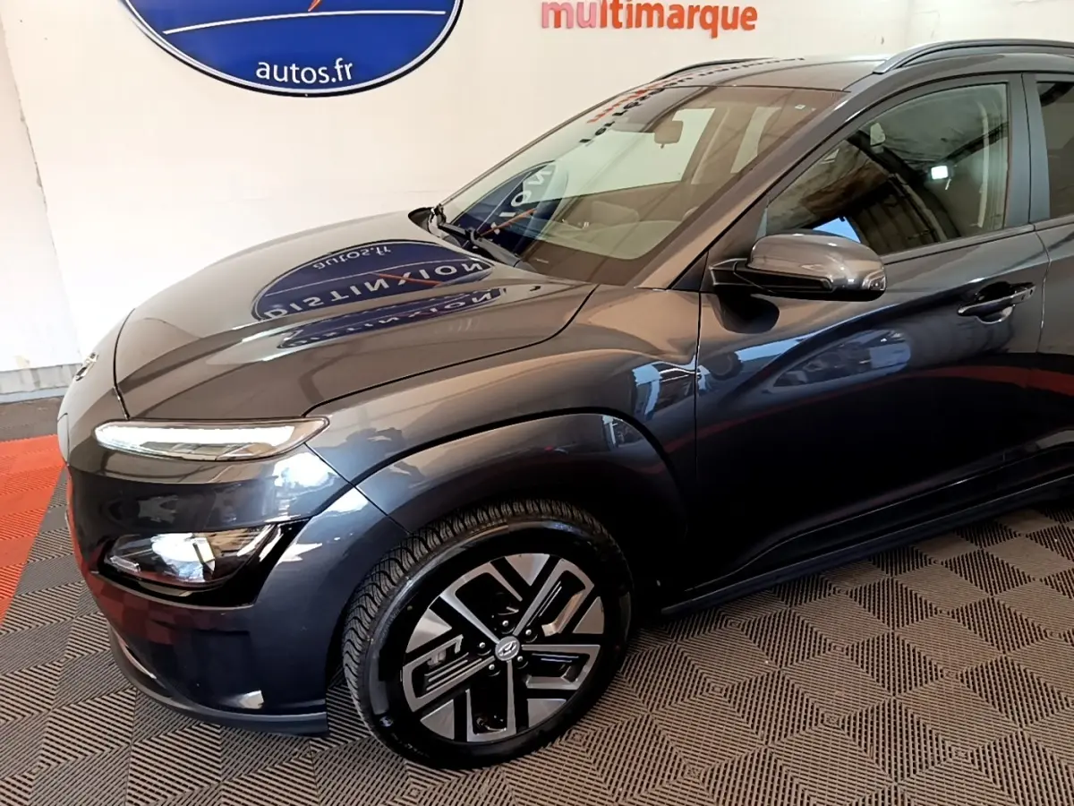 Vue 3/4 avant droit d'une Hyundai Kona électrique gris foncé avec jantes au design moderne et rétroviseurs assortis.