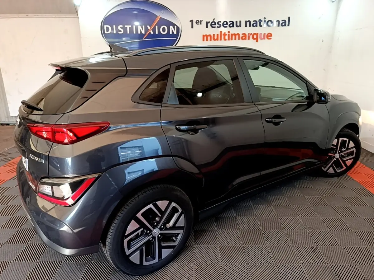 Vue 3/4 arrière droite d'un Hyundai Kona électrique gris foncé avec jantes alliage et toit noir dans un showroom.