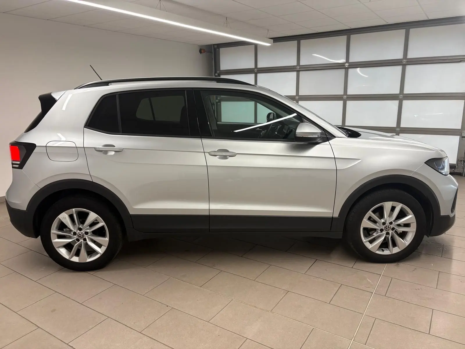 Vue de profil côté gauche d'un Volkswagen T-Cross 2024 argenté avec jantes alliage et vitres teintées.