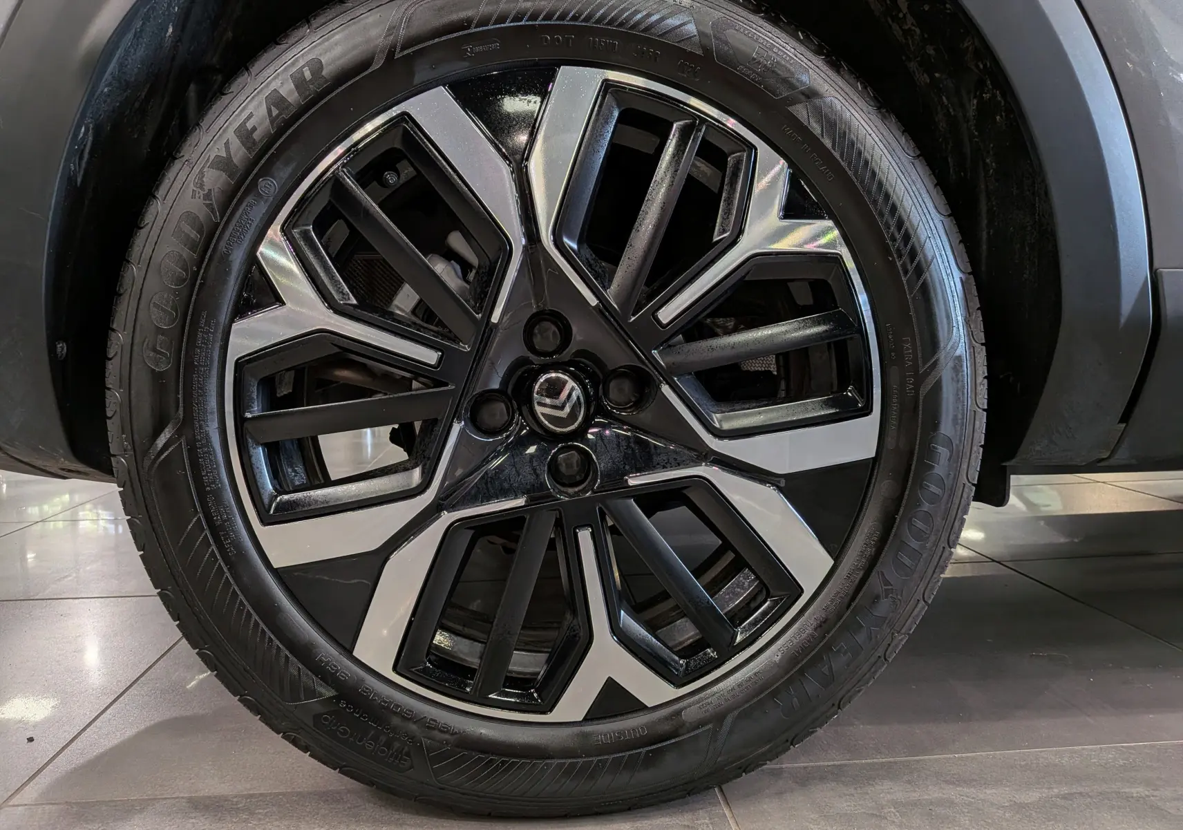 Gros plan sur la jante bicolore noire et argentée avec logo Citroën, montée sur un pneu Goodyear, partie avant droite du C4 gris Mercury.