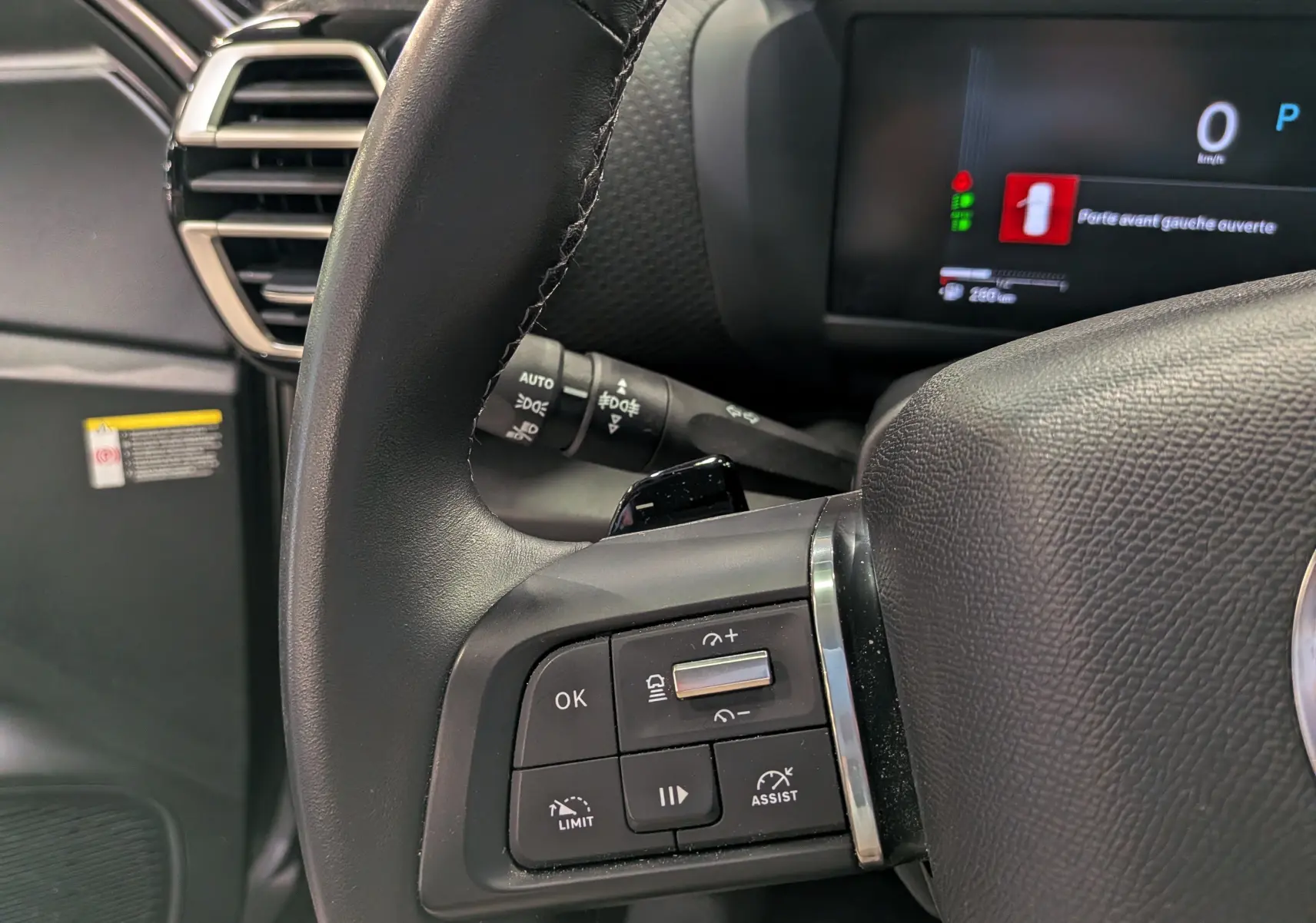 Gros plan sur le volant côté gauche de la Citroën C4 hybride 2025 avec commandes intégrées et tableau de bord numérique.