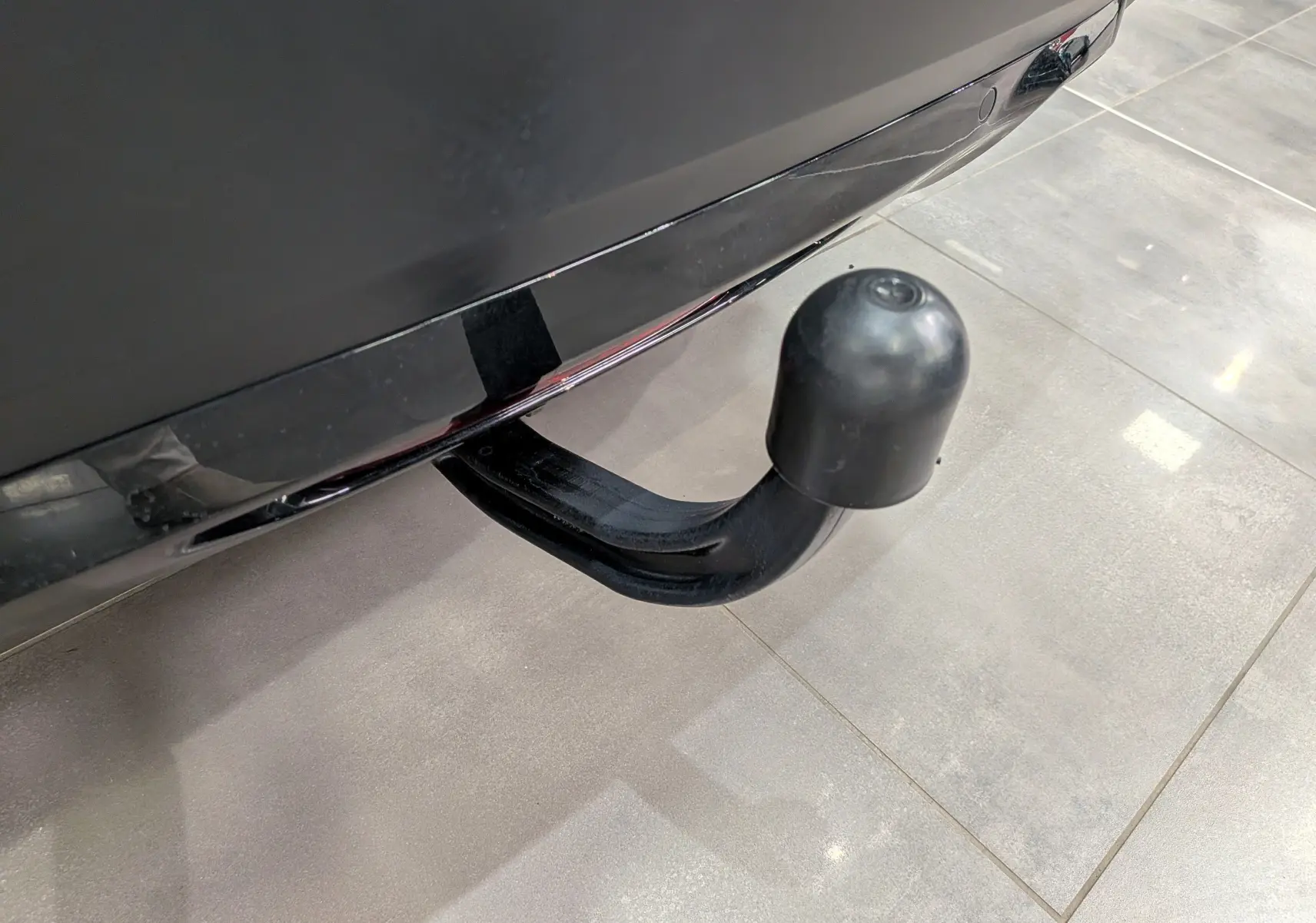 Gros plan sur l'attelage d'une Citroën C4 gris Mercury, visible sous le pare-chocs arrière sur sol carrelé.