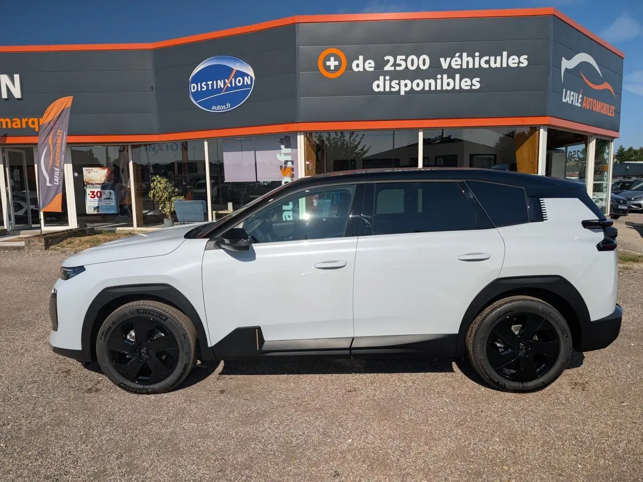 Vue latérale gauche du Citroën C5 Aircross blanc avec toit noir et jantes alliage noires, devant un concessionnaire.