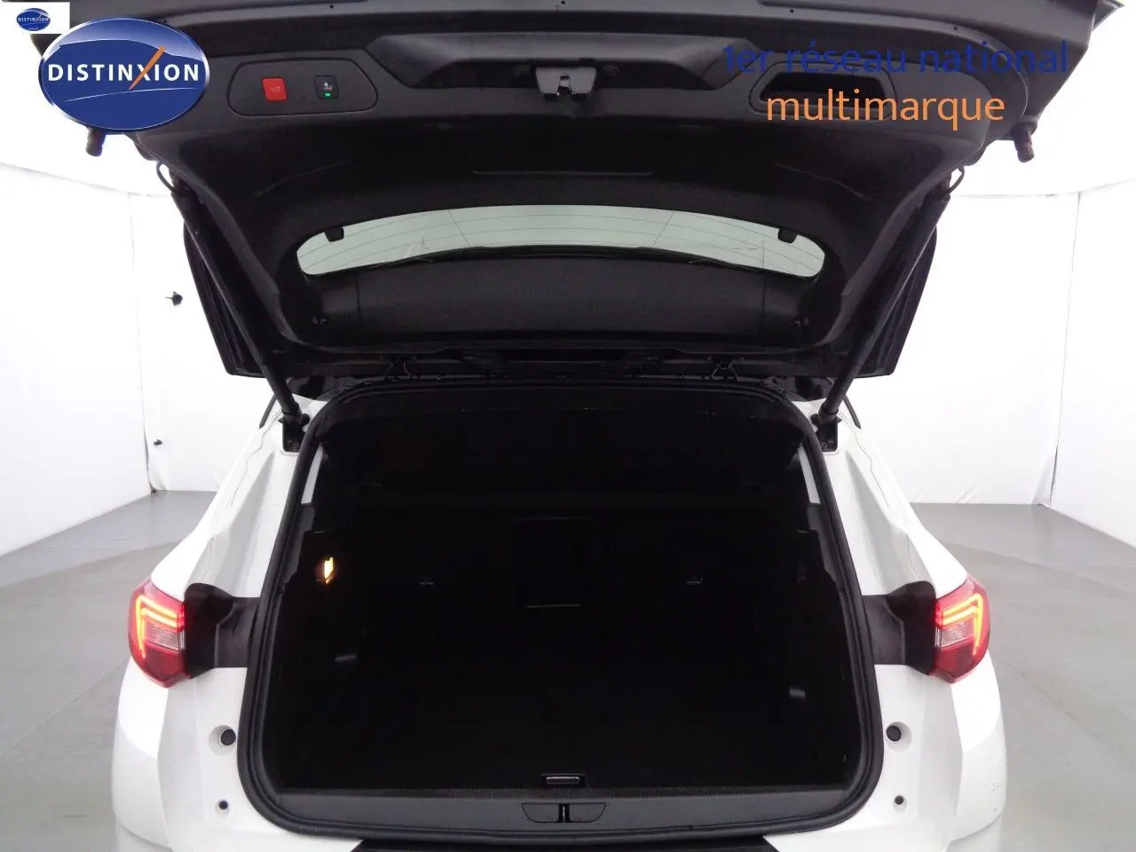 Vue arrière d'un Opel Grandland X blanc nacré avec hayon ouvert, montrant le coffre spacieux et les feux arrière allumés.