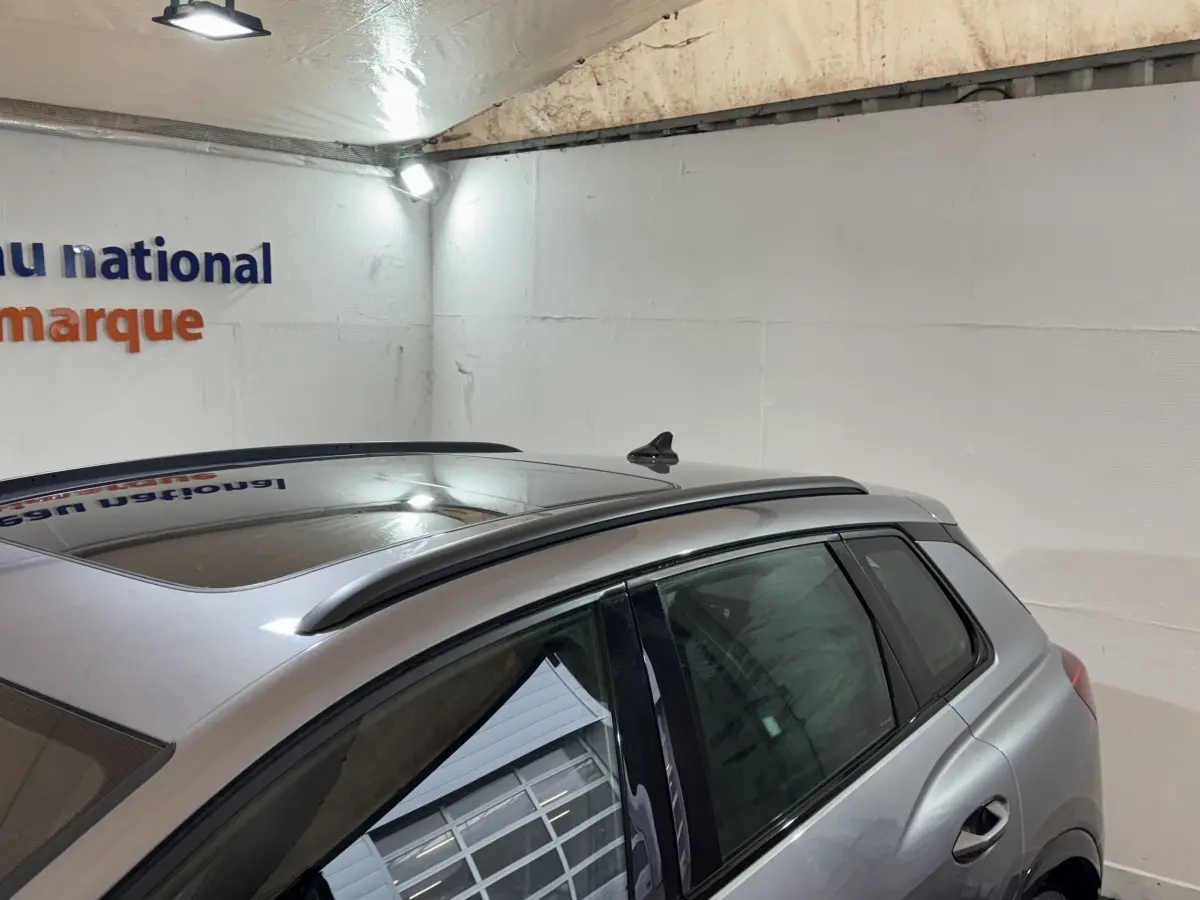 Vue arrière côté gauche d'un Audi Q4 E-TRON gris foncé avec toit panoramique et barres de toit chromées.